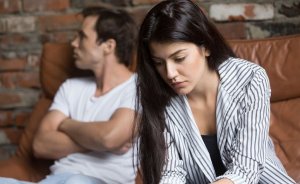 iStock Mulher desapontada e homem ao fundo com olhar distante e braços cruzados
