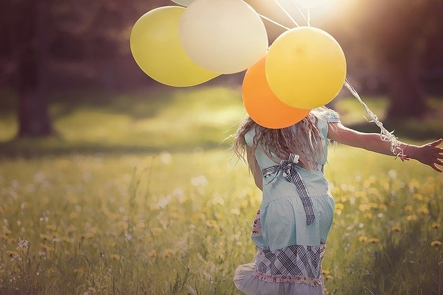 Menina correndo com balões amarelos em gramado