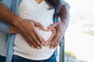 123rf. Mãos de casal formando coração em barriga de gestante.
