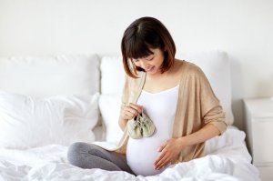 123rf. Mulher segurando sapatos de bebê ao lado de sua barriga de gestante.