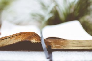 Unsplash - Ben White Bíblia aberta no meio, com duas fitas pretas, uma marcando uma página próxima ao final e a outra marca a página que está aberta.