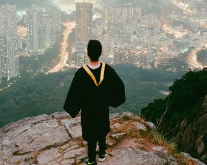 Por: Joseph Chan Aluno com roupa de formatura to topo da montanha olhando para a cidade