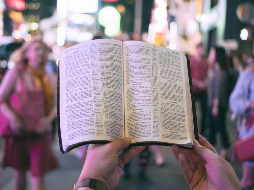 Pessoa lendo a bíblia em uma rua movimentada.