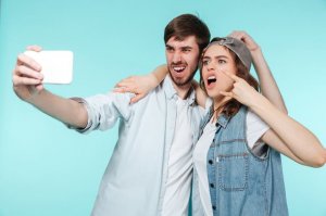 123rf. Dois irmãos, um homem e uma mulher, tirando selfie fazendo careta.