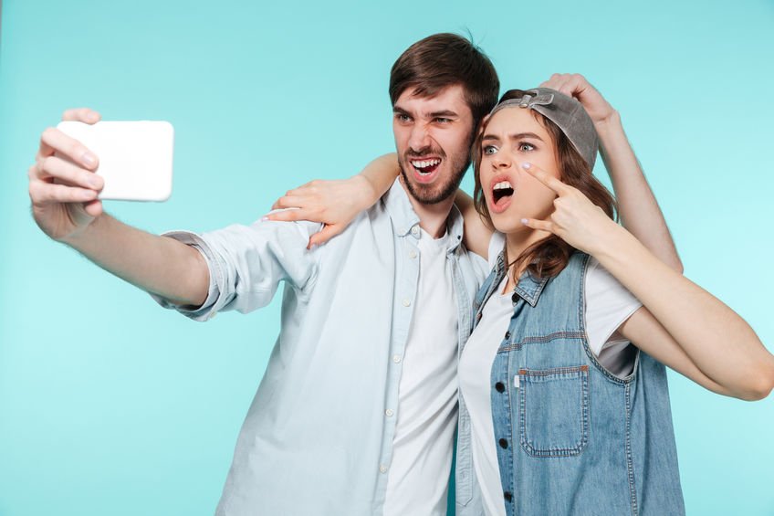 Dois irmãos, um homem e uma mulher, tirando selfie fazendo careta.