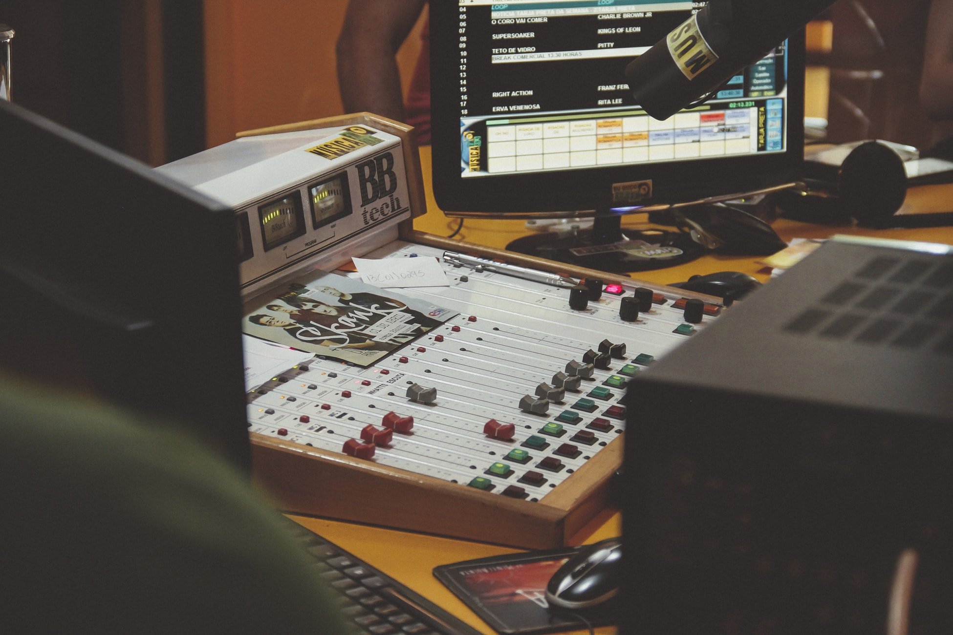 Mesa de som, monitor e microfone em estúdio de rádio.