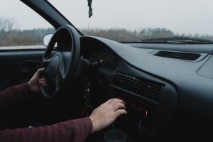 Unsplash - Courtney Corlew Pessoa dirigindo carro, enquanto mexe no rádio no painel.
