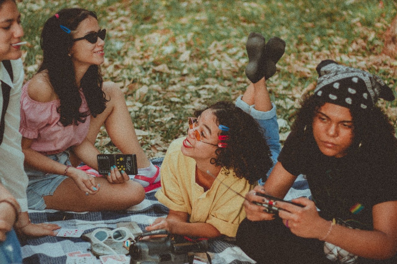 Quatro meninas sentadas em toalha em gramado, ouvindo música em um rádio portátil.