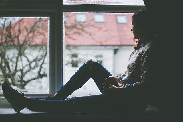 Menina sentada em parapeito de janela com as pernas esticadas