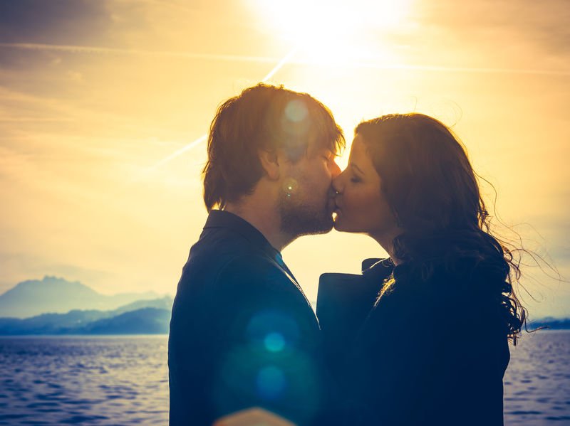 Casal se beijando ao lado de um mar em um dia ensolarado.