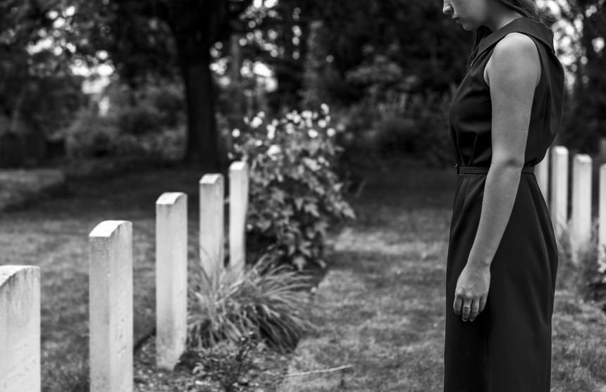 Mulher parada diante de túmulo em cemitério.