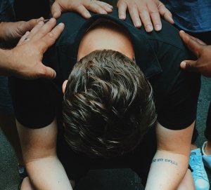 Jon Tyson - Unsplash Homem apoiando seus braços na perna enquanto mãos de outras pessoas estão em suas costas