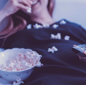 JESHOOTS.COM - Unsplash Mulher comendo pipoca enquanto segura controle da televisão