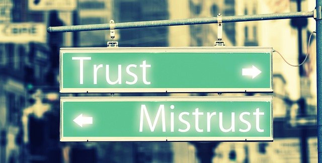 Placa com setas indicando direções opostas com as palavras 'Trust' (confiança) e 'Mistrust' (desconfiança)