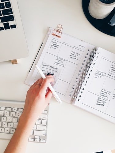 Mão com caneta, caderno e teclado sobre mesa