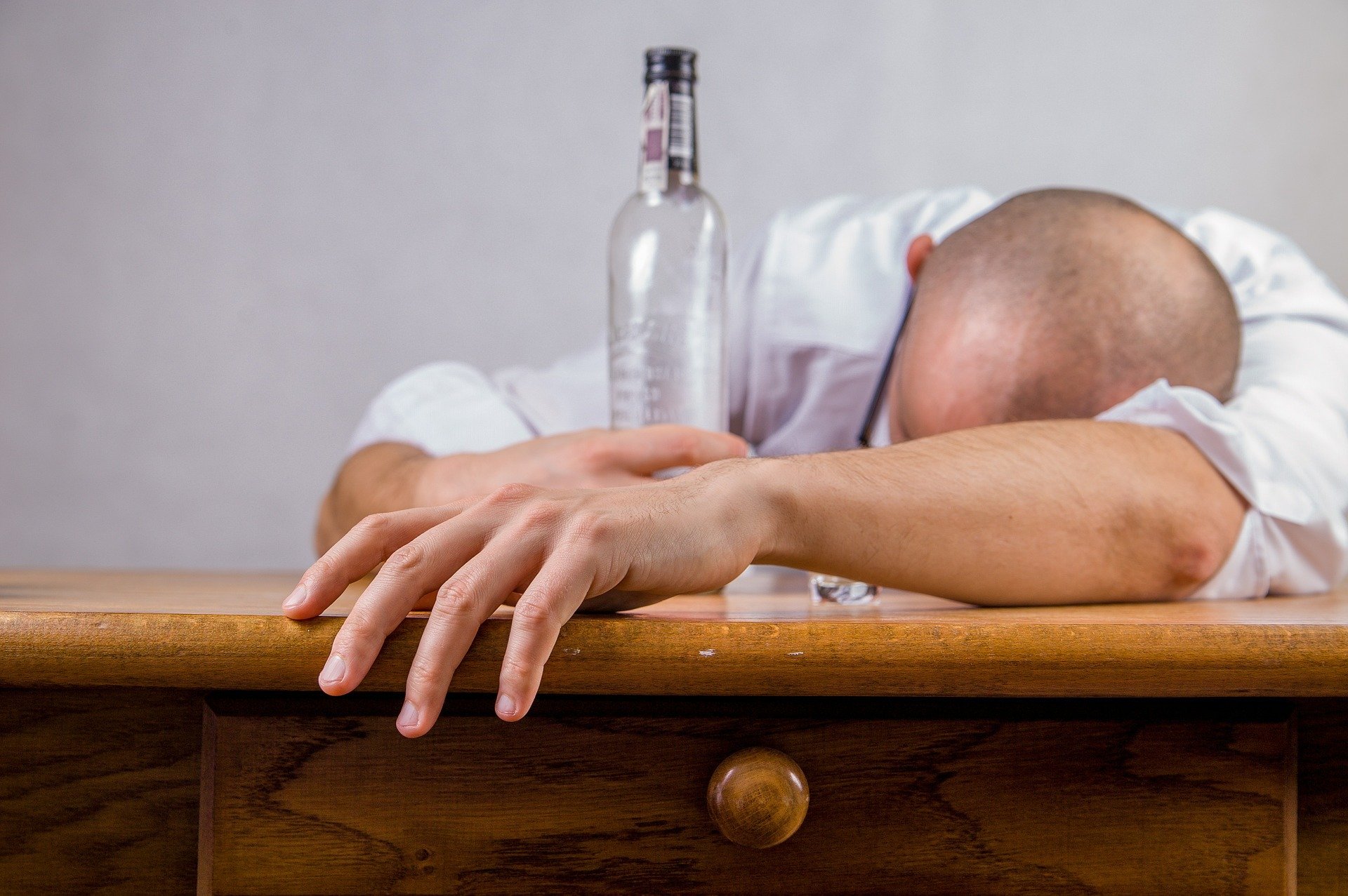 Homem deitado na mesa segurando garrafa