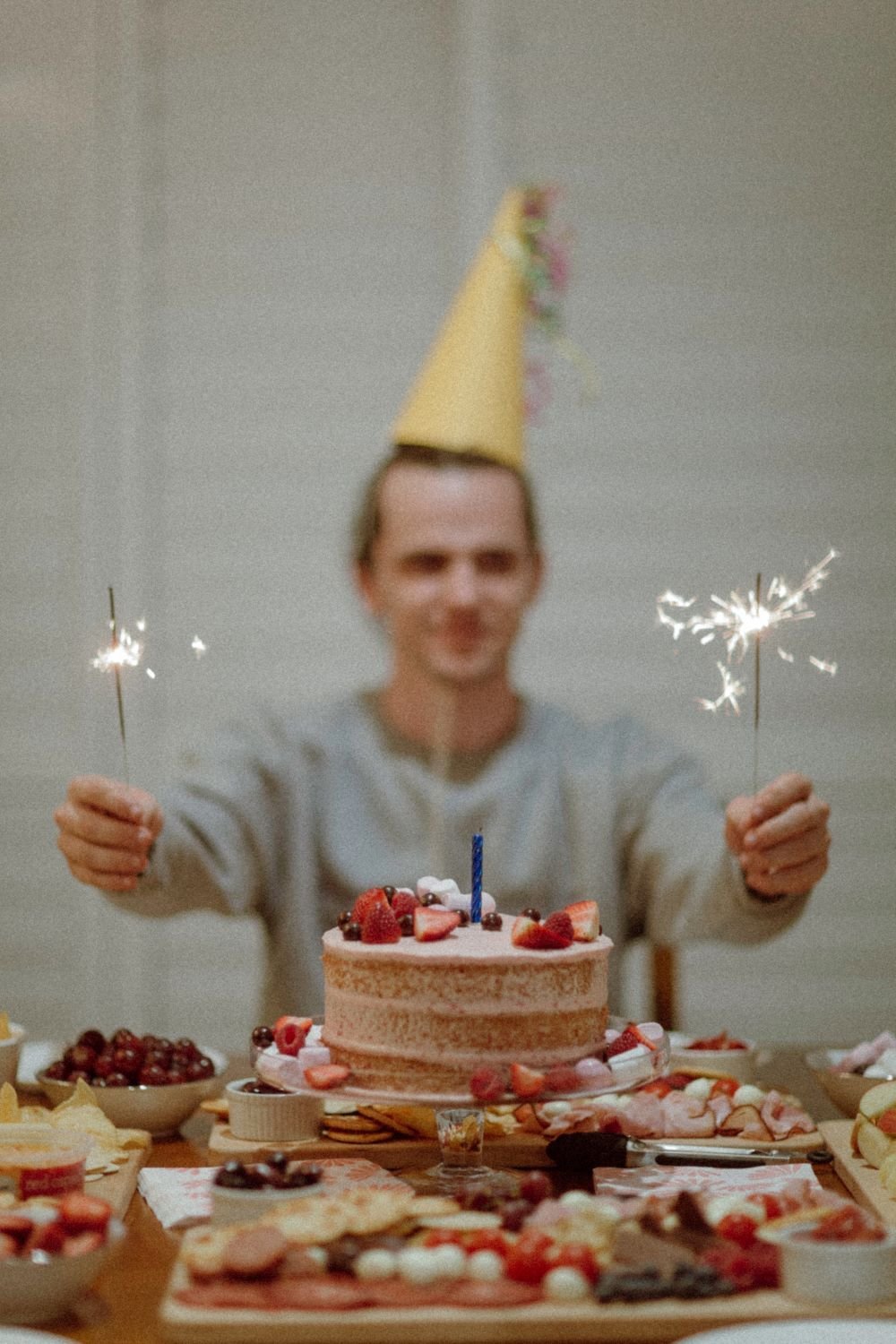 Homem com chapéu de aniversário segurando velas sobre seu bolo.