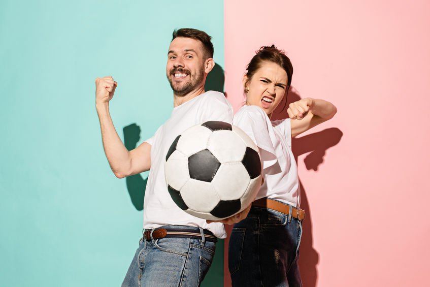 Homem e mulher comemorando com uma bola de futebol na frente.