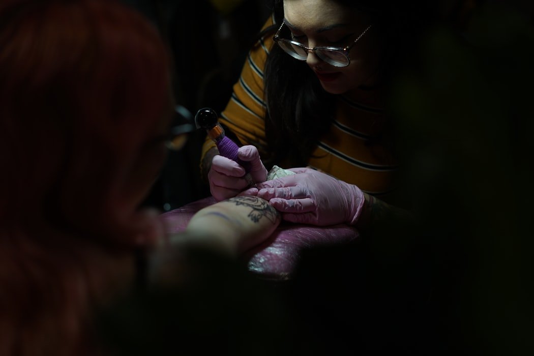 Mulher tatuadora trabalhando no antebraço de uma pessoa.