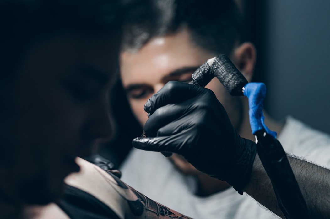 Homem segurando aparelho de tatuagem com uma luva.
