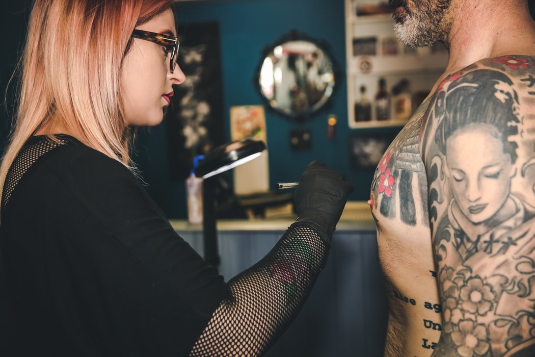 Mulher tatuadora desenhando na pele de um homem tatuado, em um estúdio.