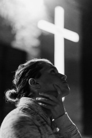 Unsplash/KEEM IBARRA Mulher pensativa com cruz ao fundo