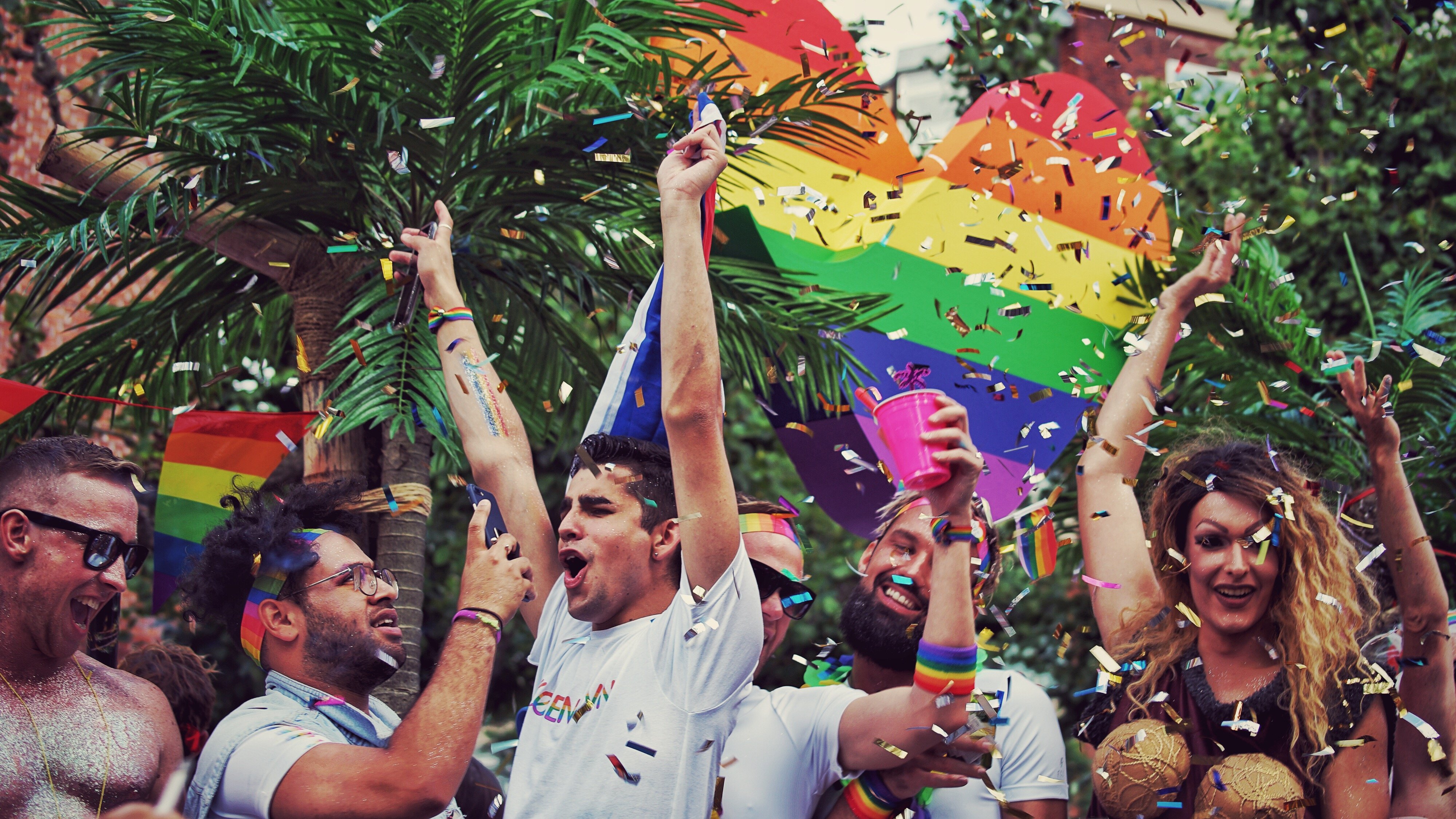 Grupo de pessoas dançando, cantando e sorrindo com bandeiras de arco iris