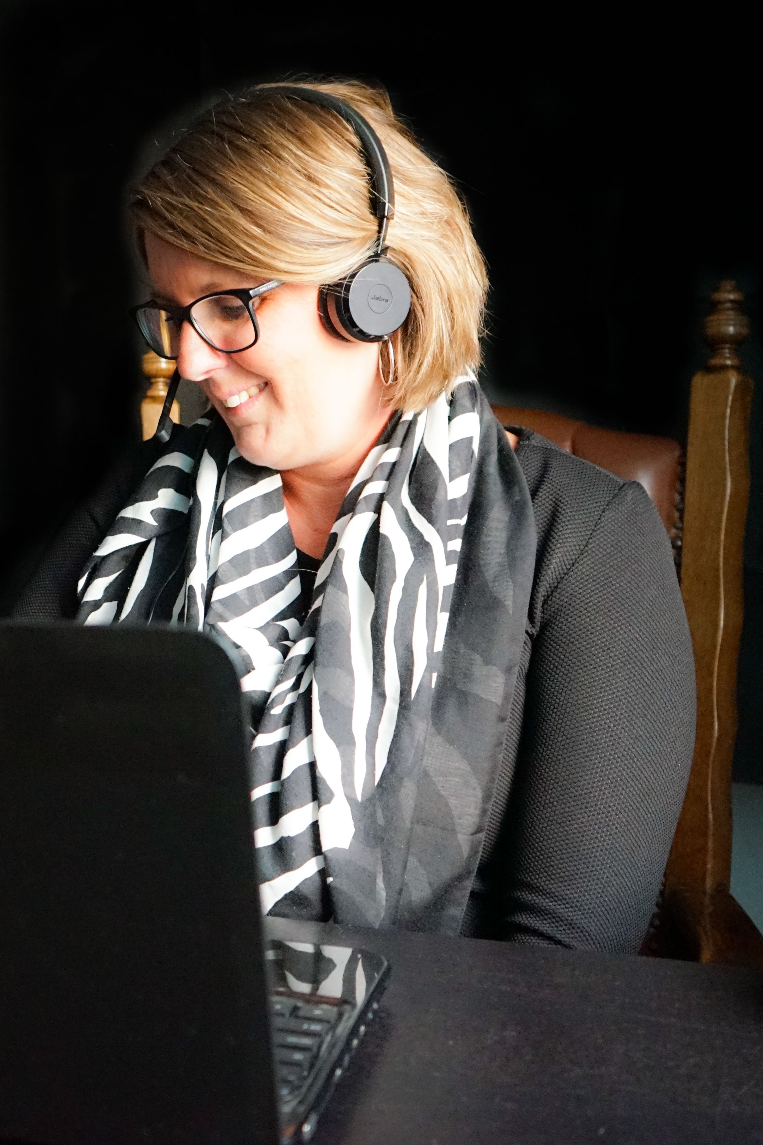 Mulher com fones de ouvido sorrindo com um computador em sua frente