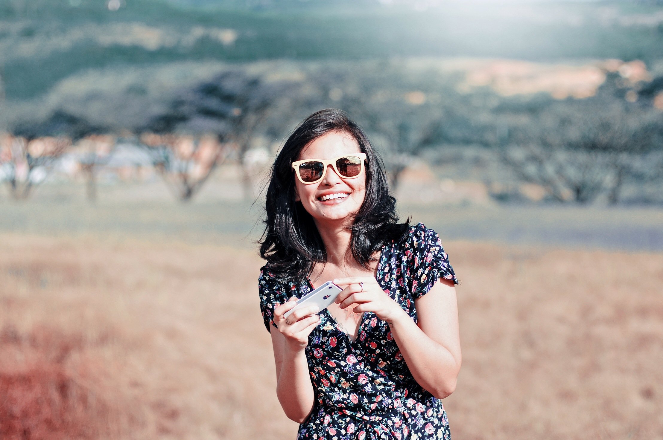 Mulher sorrindo em campo aberto com celular na mão