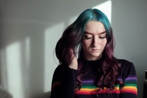 Sharon McCutcheon/Unsplash Garota com o olhar para baixo ao lado de uma janela.