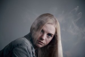 Sharon McCutcheon/Unsplash Mulher parada enquanto sobe uma fumaça ao lado do seu rosto.