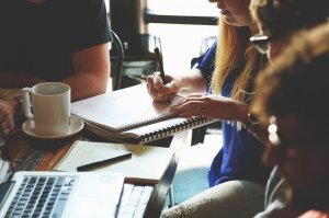 Pixabay/StartupStockPhotos Pessoa escrevendo em caderno com colegas em volta