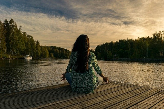 Mulher sentada e meditando em frente ao rio