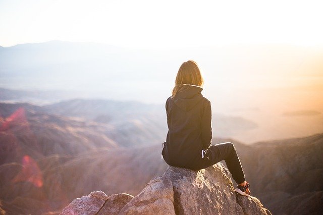 Menina sentada em pedra olhando para o horizonte