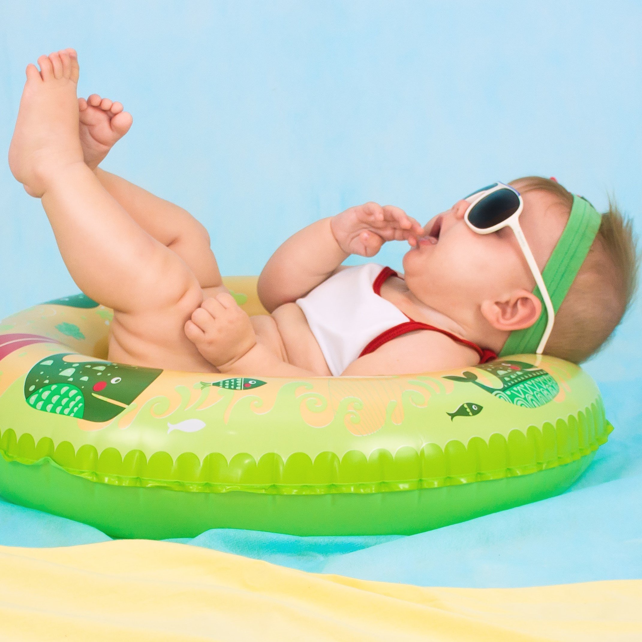 Bebê deitado em boia da piscina com óculos de sol