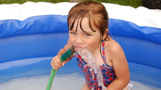 Criança na piscina com a mangueira de água na boca