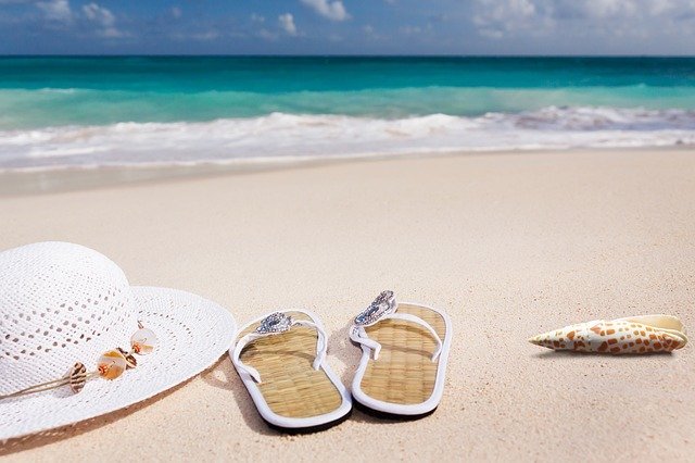 Chinelo e chapéu na areia em frente ao mar