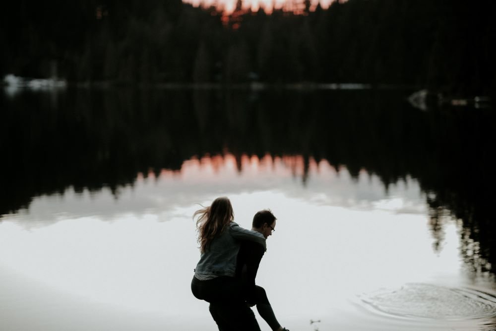 Mulher nas costas de um homem na beira de um lago.