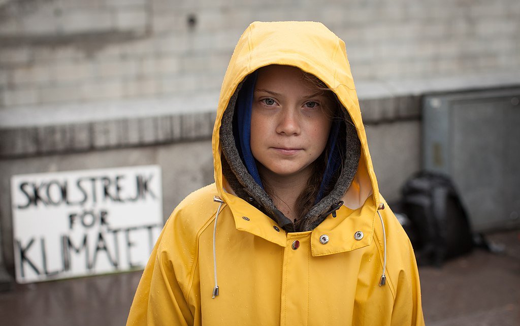 Greta Thunberg usando capa de chuva amarela em protesto na frente do Parlamento Sueco.