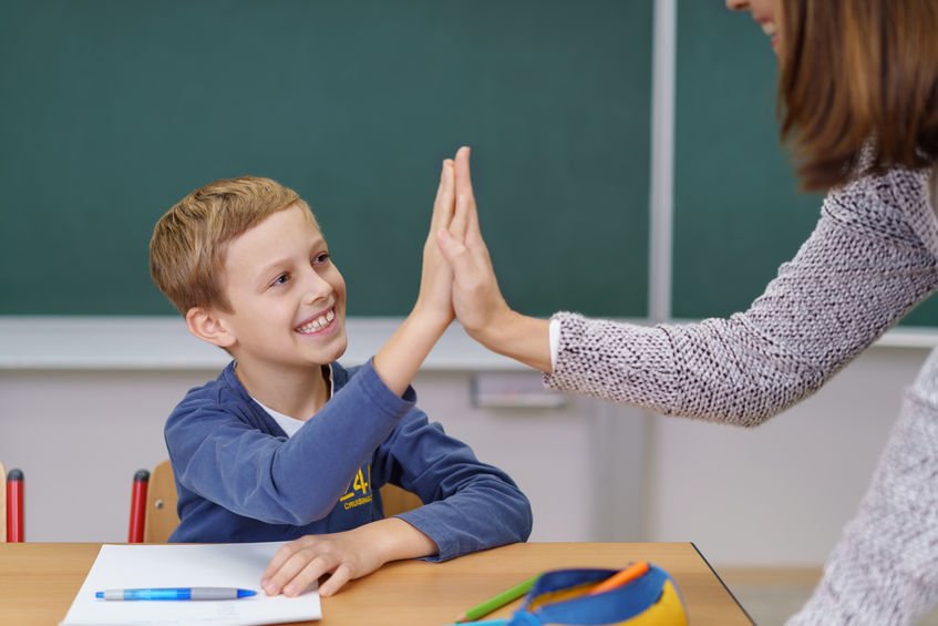 Professora e aluno sorridente batendo suas mãos.