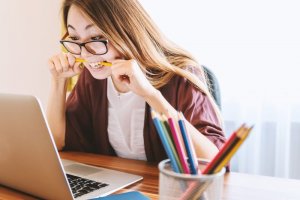 Jeshoots/Unsplash Garota nervosa mordendo um lápis olhando para a tela do notebook.