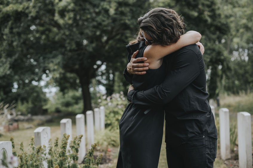 Pessoas de luto se abraçando em cemitério