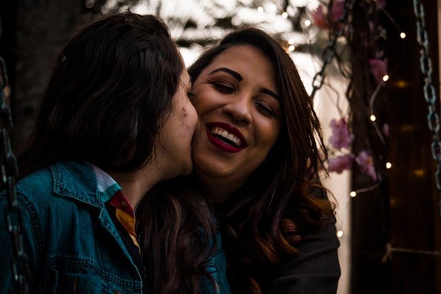 Mulher beijando a bochecha de outra mulher