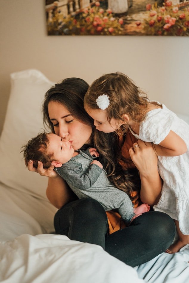 Mulher abraçada com seus dois filhos crianças na cama.