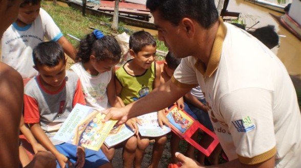 Homem entregando livros infantis com histórias bíblicas para um grupo de crianças.