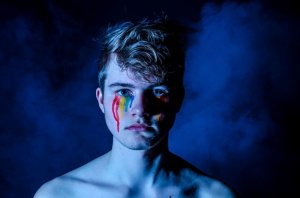 Christian Sterk/Unsplash Garoto com a cara pintada em cores do arco-íris escorrendo abaixo dos olhos.