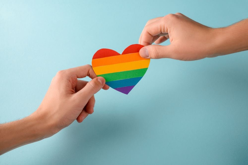 Duas mãos segurando um coração com as cores do arco-íris.