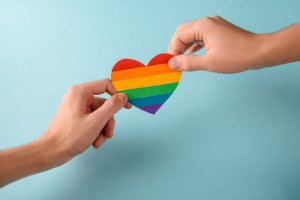 123rf Duas mãos segurando um coração com as cores do arco-íris.