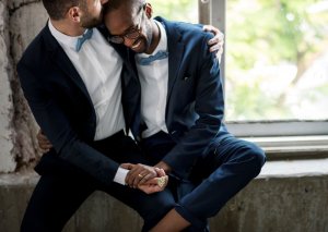 123rf casal de homens sentados próximos a uma janela. Um está beijando a cabeça do outro.