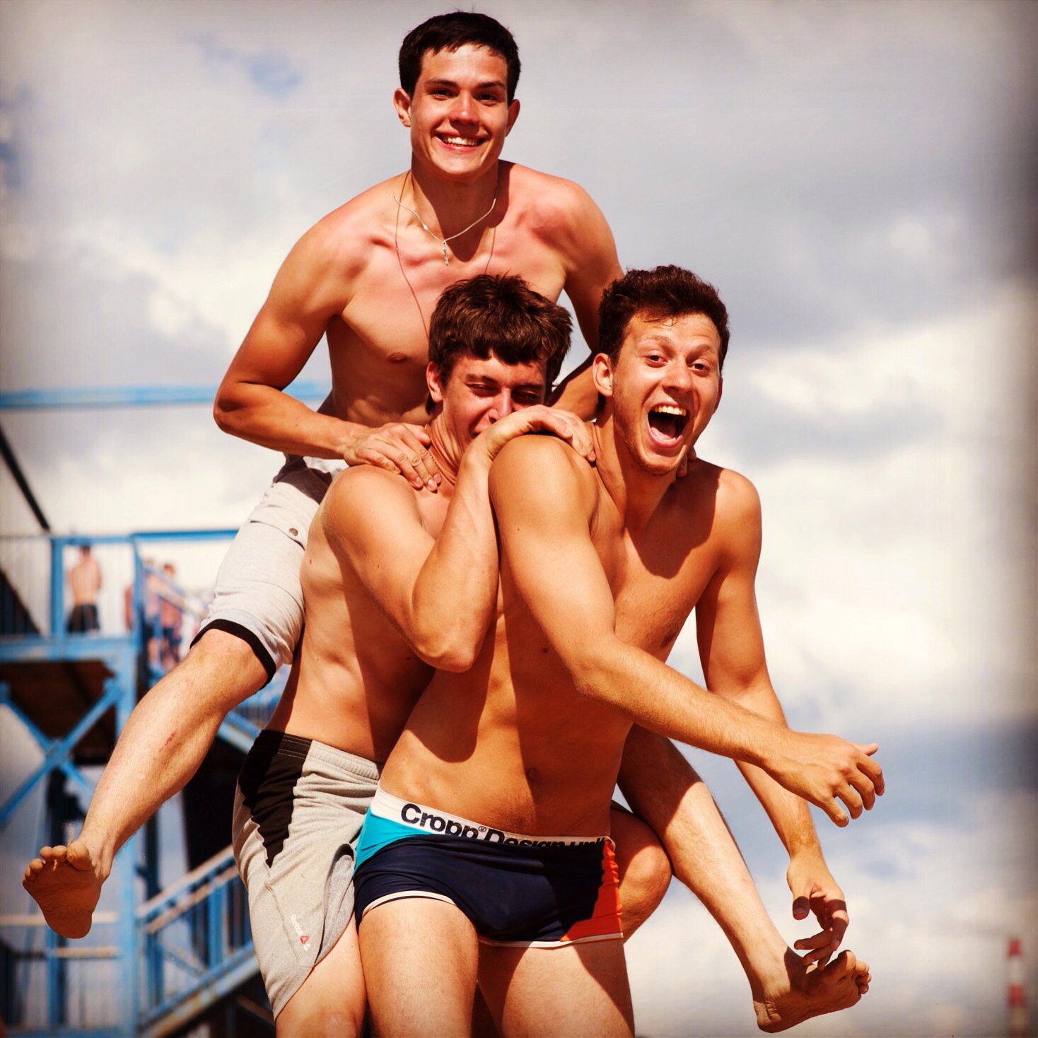 Três homens pulando em cima do outro na praia